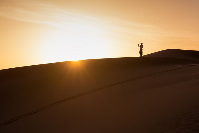 A lone walker on an Erg Chebbi dune crest at sunset
